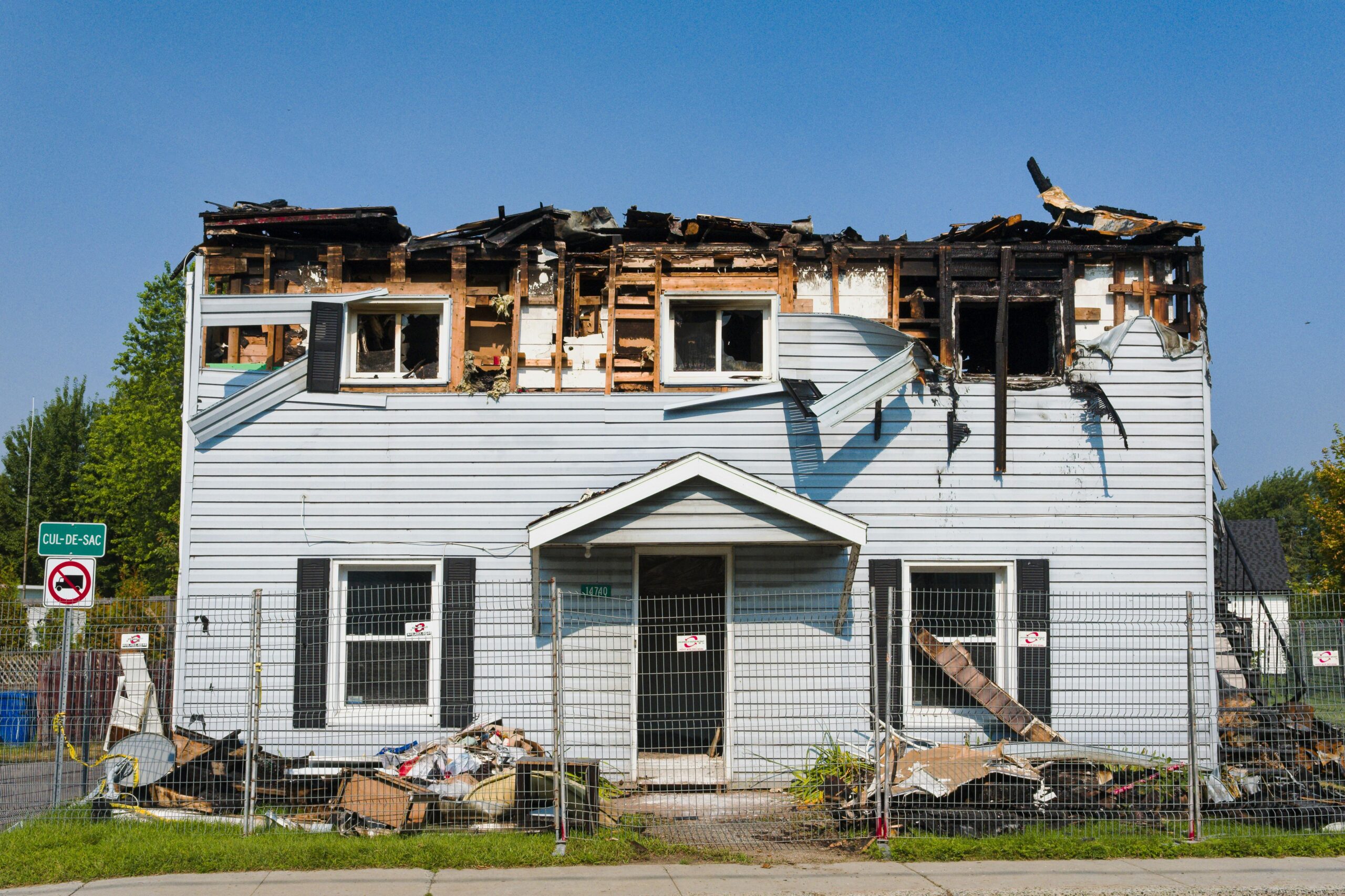 A damaged house with a burnt roof in Bécancour, Quebec, surrounded by a fence.