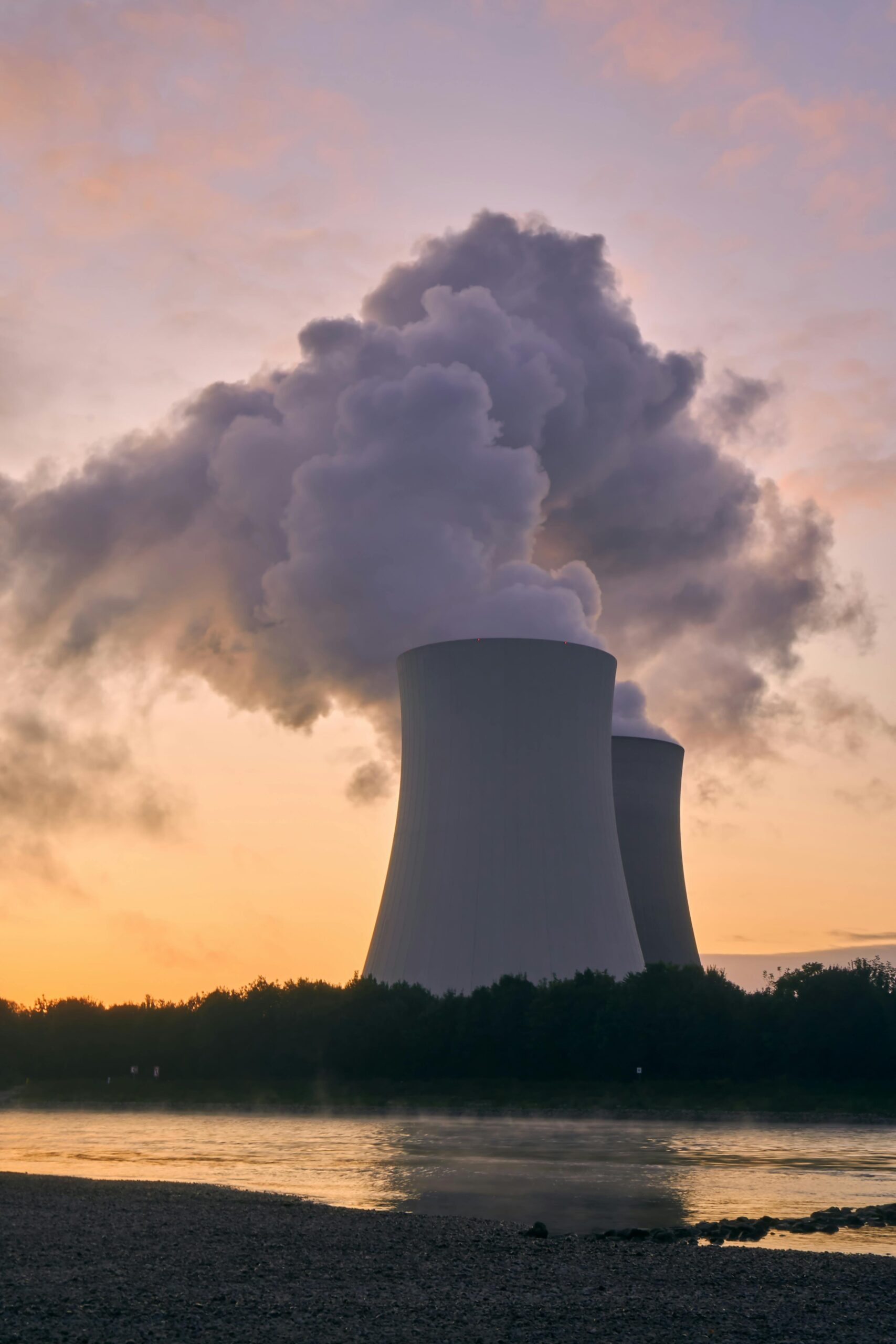 Silhouette of a nuclear power plant emitting steam during a colorful sunset.